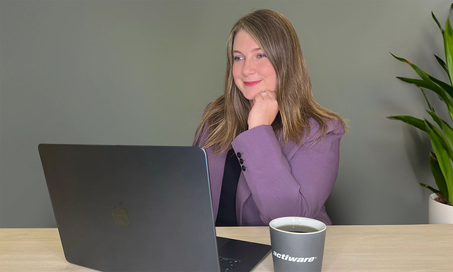 Eine Mitarbeiterin sitzt im Büro an ihrem Laptop und blickt mit einem zufriedenen Lächeln auf den Bildschirm.